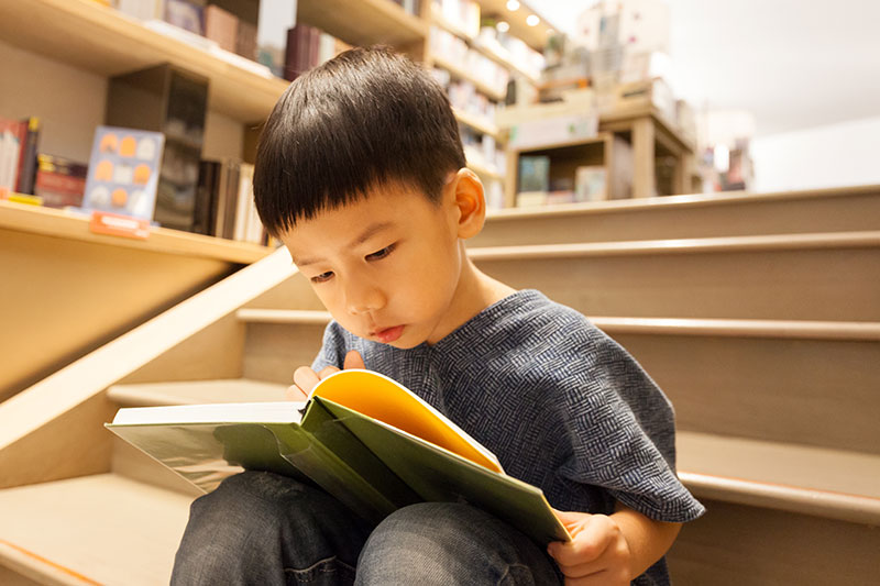 young boy reading looking closely at book 