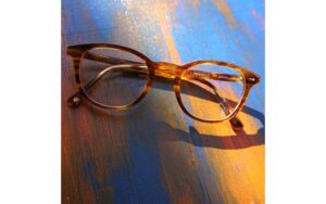 A pair of tortoiseshell eyeglasses rests on a textured surface painted with blue and orange hues, casting a shadow. The words "unique & unlimited" are visible on the frame.