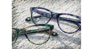 Two pairs of multicolored eyeglasses with patterned frames are placed on a textured gray surface, capturing sunlight.